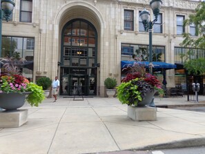 A building with a large arched entrance, outdoor seating, and potted plants.