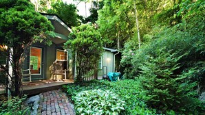 A house with a brick pathway leading to a porch, surrounded by lush greenery and trees.