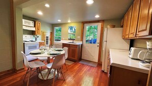 A compact kitchen with wooden cabinets, a dining table set for four, and a refrigerator.