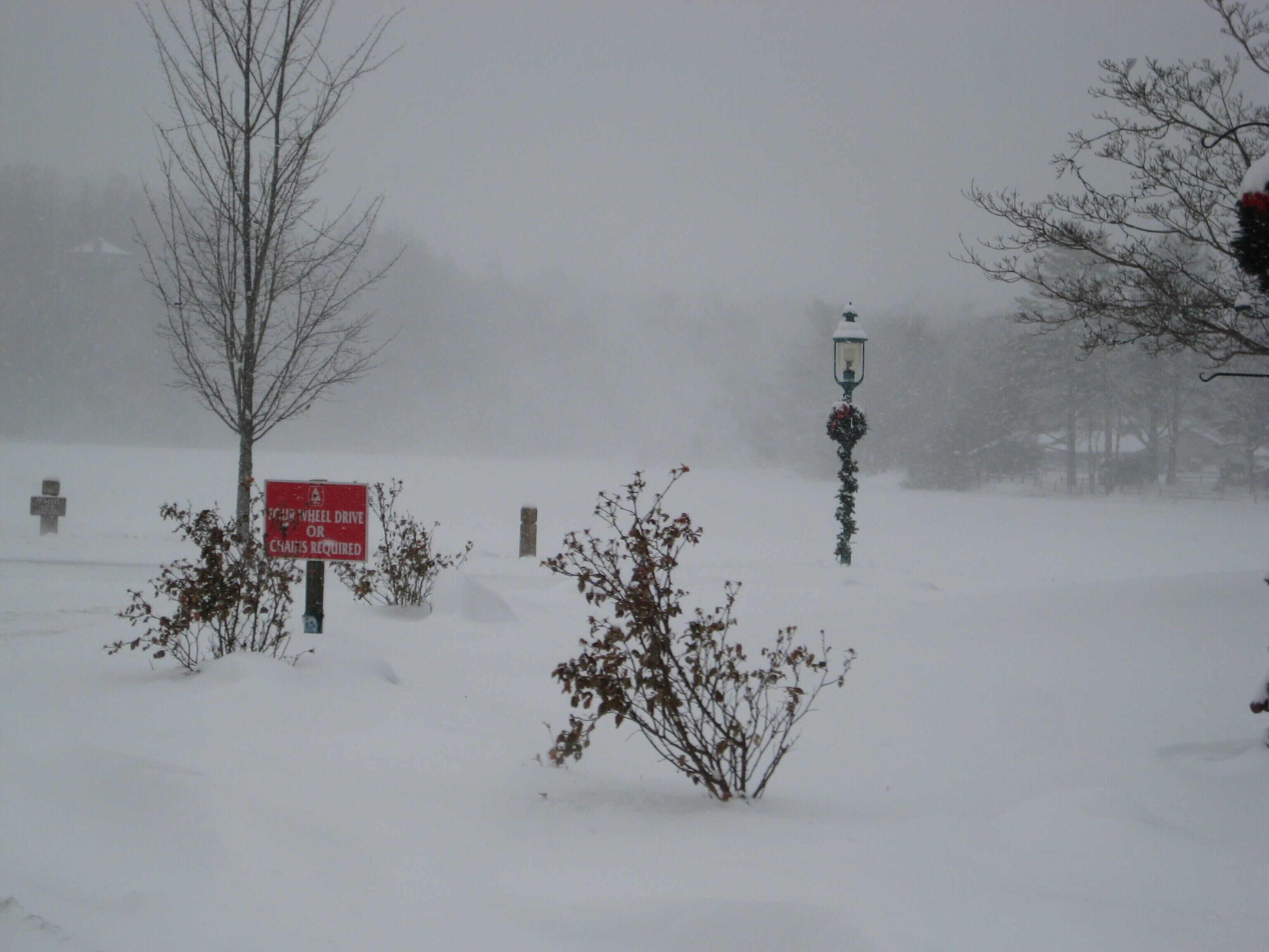 A snowy scene with a sign indicating a wheel drive or chains required for vehicles.