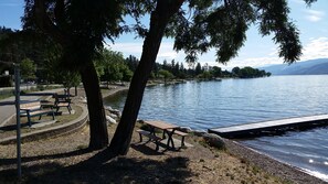 A lakeside park with benches and picnic tables, a walking path, and a dock extending into the water. - Peachland Treehouse Suite (Peachland)