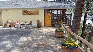 A building with a wooden sign reading "Peachland Eagles Nest B&B," outdoor seating with chairs and tables, and flower planters. - Peachland Treehouse Suite (Peachland)