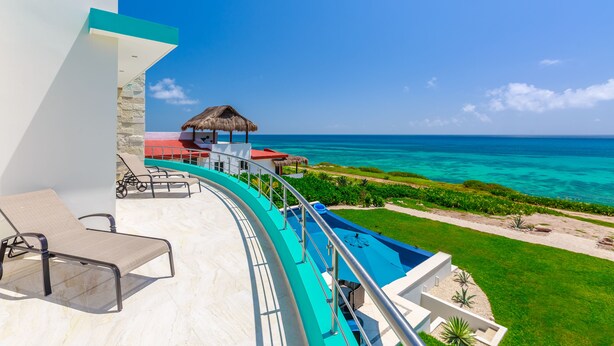 A poolside area with lounge chairs, a thatched-roof structure, and a view of the ocean. - Casa Flor de Mayo  5BR Villa with Infinity Pool & Stunning Ocean Views (Isla Mujeres)