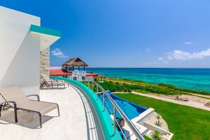 A poolside area with lounge chairs, a thatched-roof structure, and a view of the ocean. - Casa Flor de Mayo  5BR Villa with Infinity Pool & Stunning Ocean Views (Isla Mujeres)