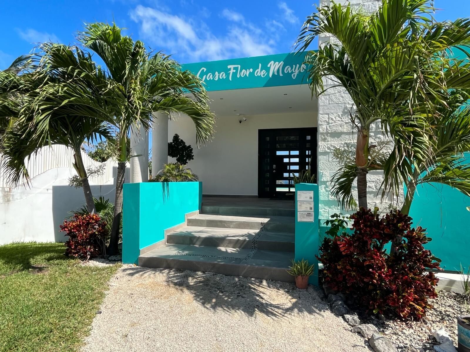 The entrance to Casa Flor de Mayo with a clear blue sky, palm trees, and a turquoise awning.