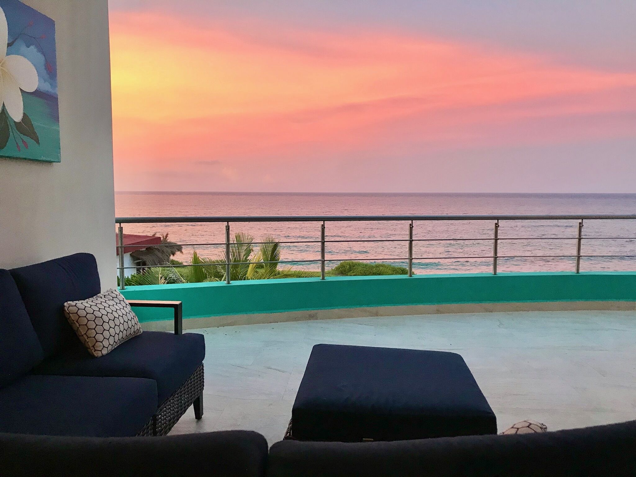 A balcony with a view of the ocean at sunset, featuring a sofa and a small table.