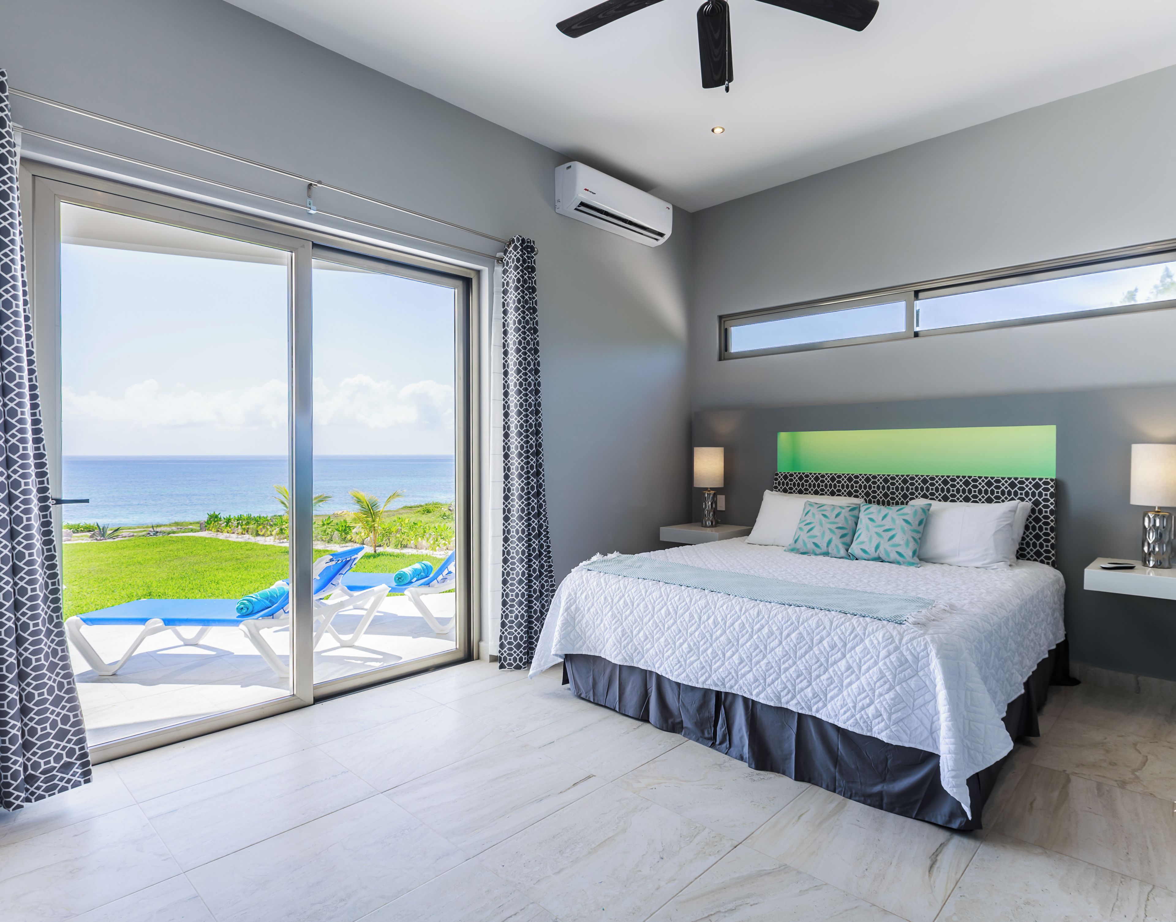 A bedroom with a large bed, a view of the ocean, and a ceiling fan.