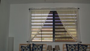A bedroom with two beds, a nightstand with lamps, and a window with blinds. - Dos Palmas-3Bdrm, 2Ba, Walk One Block to Caribbean,Malecon,restaurants,etc (Vieques)
