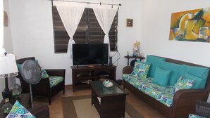 A living room with a sofa, a television, a fan, and a coffee table. - Dos Palmas-3Bdrm, 2Ba, Walk One Block to Caribbean,Malecon,restaurants,etc (Vieques)