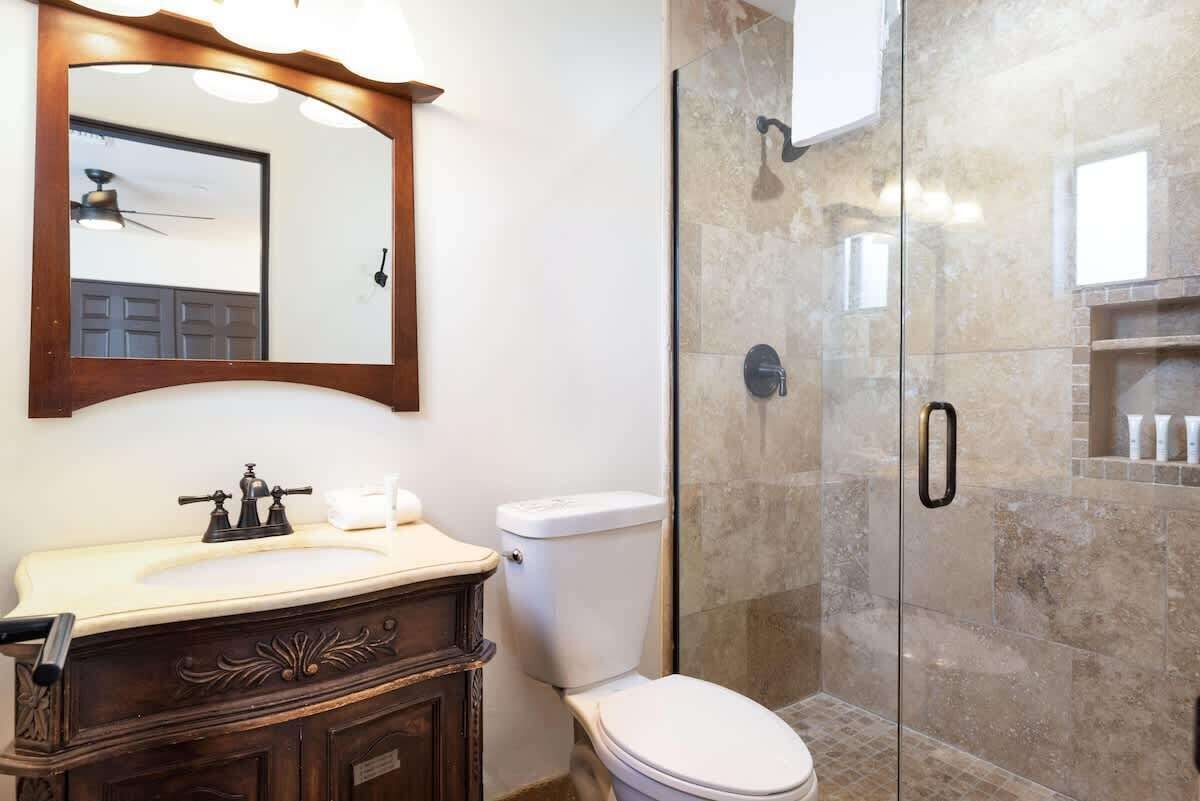A bathroom with a wooden vanity, a white toilet, a glass-enclosed shower, and a mirror above the vanity.