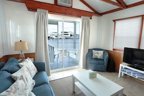 A living room with a blue sofa, a white coffee table, a television, and a view of a marina through a glass door. - Waterfront Sunset View Aqua Villa at Conch Shell @ Mangrove Resort LLC (Tavernier)