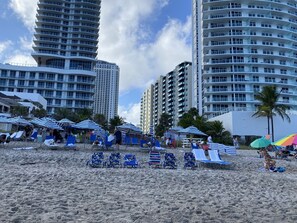 Una playa con filas de sillas y sombrillas, rodeada de altos edificios residenciales.