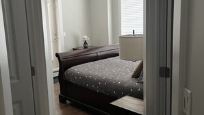 A bedroom with a bed, a dresser, a window with blinds, and a door. - Beautiful Downtown Executive Suite (Edmonton)
