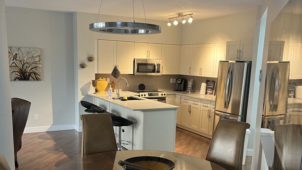 A modern kitchen with a central island, stainless steel appliances, and a dining area with a round table and chairs. - Beautiful Downtown Executive Suite (Edmonton)