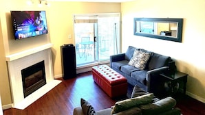 Una sala de estar con chimenea, televisor montado en la pared, un sofá y puerta corrediza de vidrio que da a un espacio exterior.