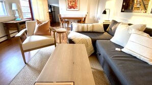A living room with a sofa, chairs, a wooden coffee table, and a dining area with a table and chairs. - Secluded 1 Br Cottage on the Lake, Close to Ditch with OS Shower & Fabulous Yard (Montauk)