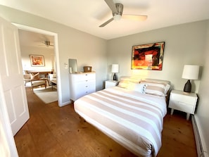 Una camera da letto con un letto grande, un ventilatore a soffitto, un comodino con una lampada e un quadro appeso al muro.