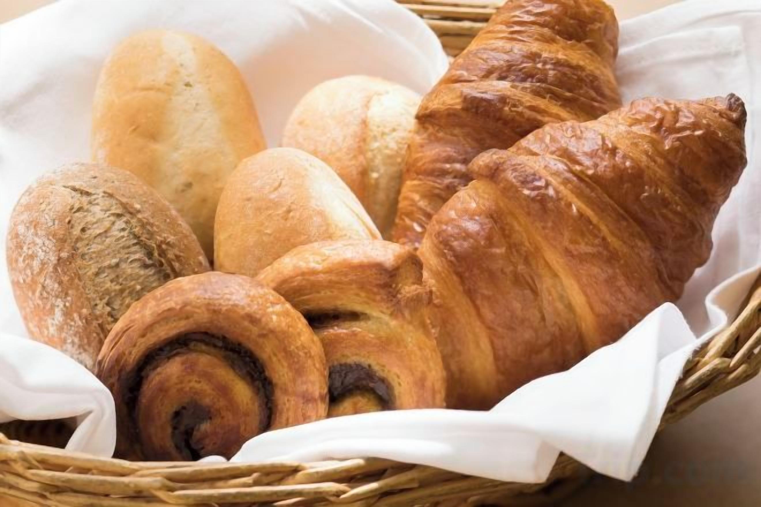 A basket containing various types of bread, including a croissant and a baguette.