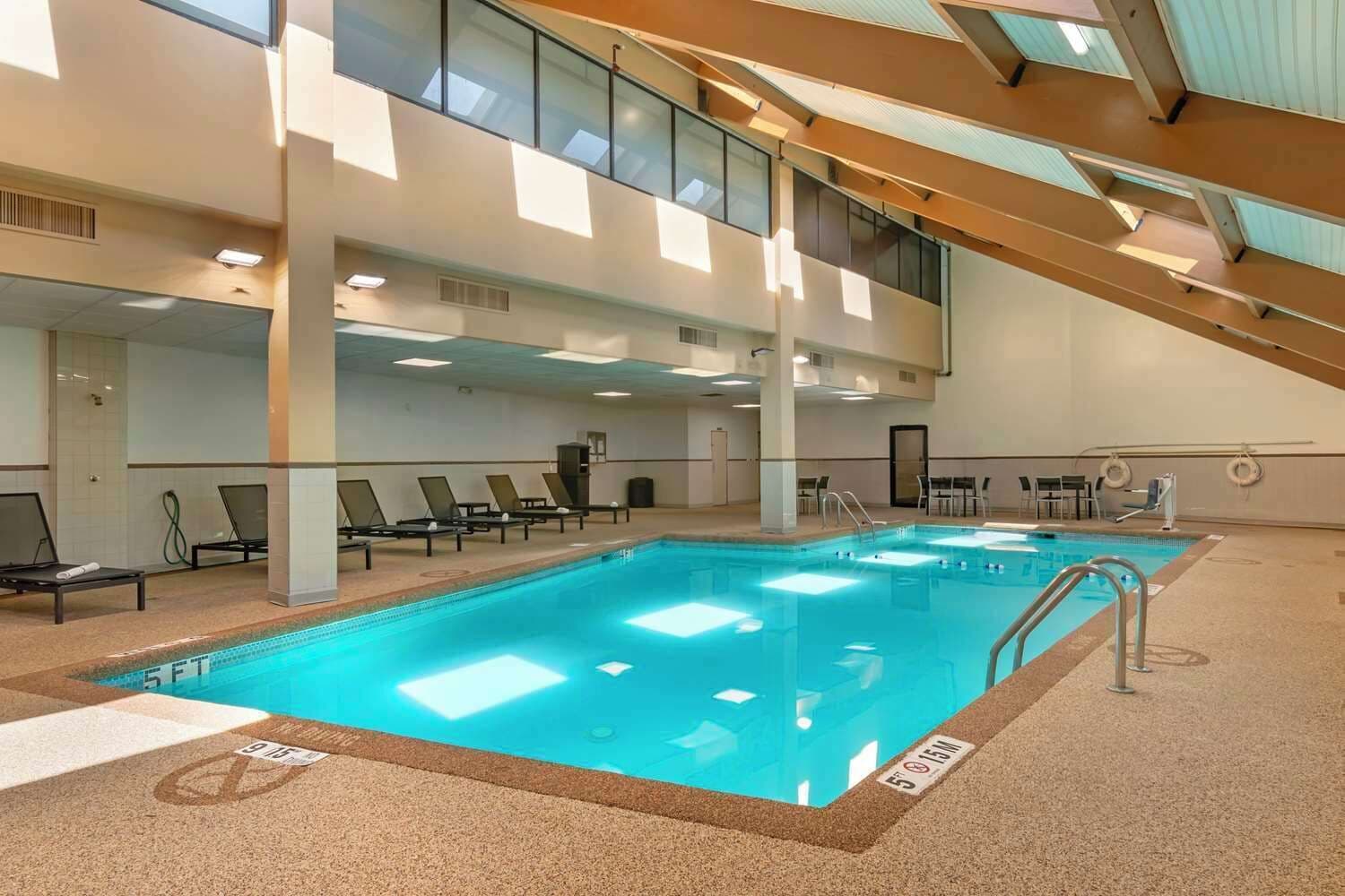 A large indoor swimming pool with multiple lounge chairs and a high ceiling with skylights.