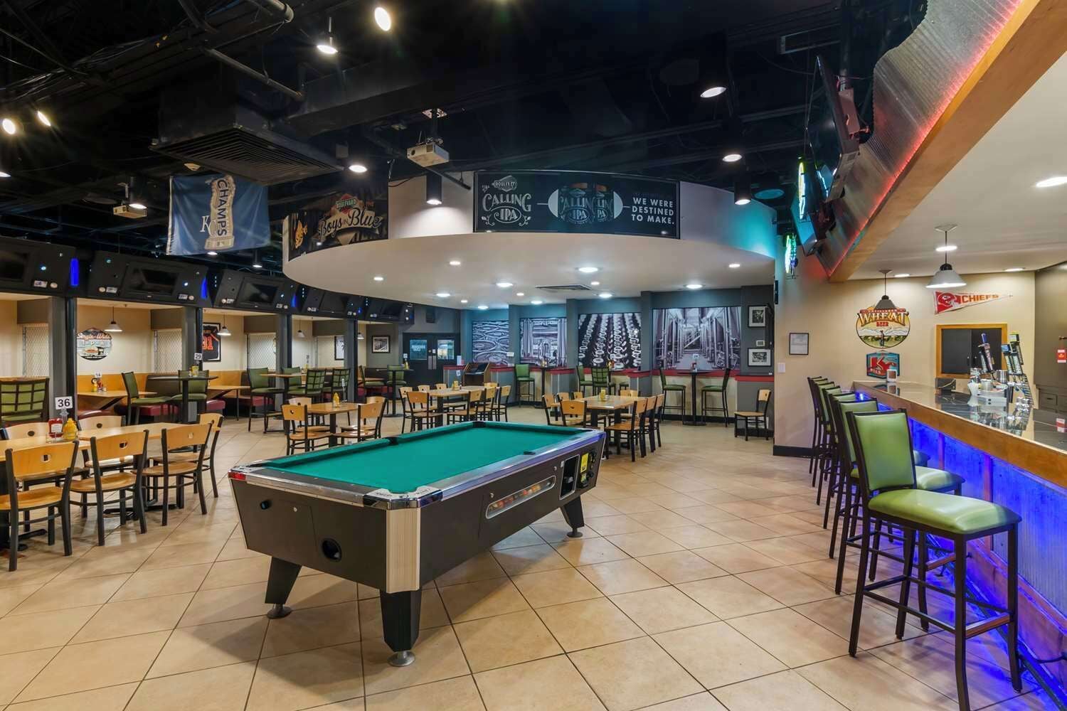 Une salle de billard avec plusieurs tables de billard, une table de pool et un espace bar.