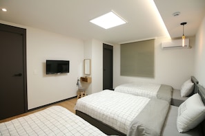 A hotel room with two beds, a television, a mirror, a window with blinds, and an air conditioning unit.