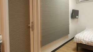 A modern hotel room with a sliding door, a large window with blinds, a bed with a checkered bedspread, and an air conditioning unit on the wall. - Heima Guesthouse Hongdae (Seoul)
