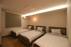 A bedroom with two beds, each with a headboard and a pillow with text. There is a window with blinds, a ceiling light, and an air conditioning unit.
