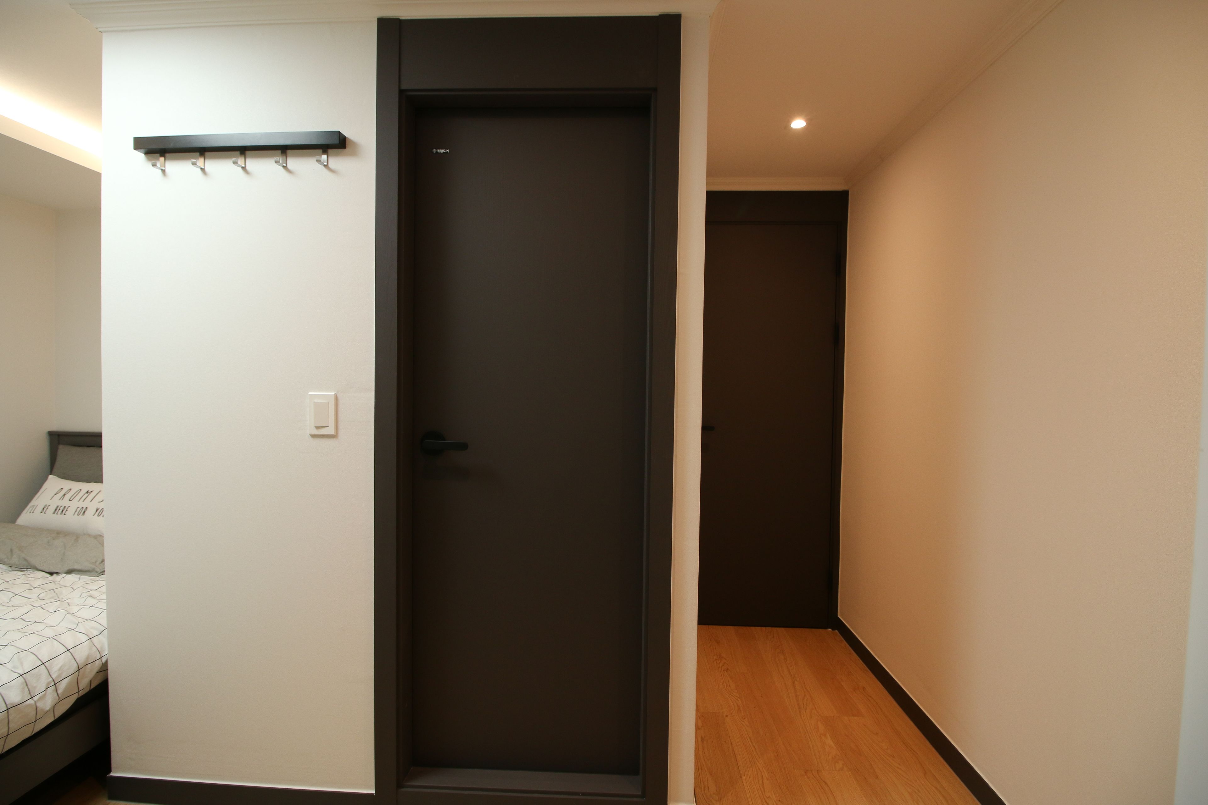 A bedroom with a bed, a dark door, a coat rack, and a wooden floor.