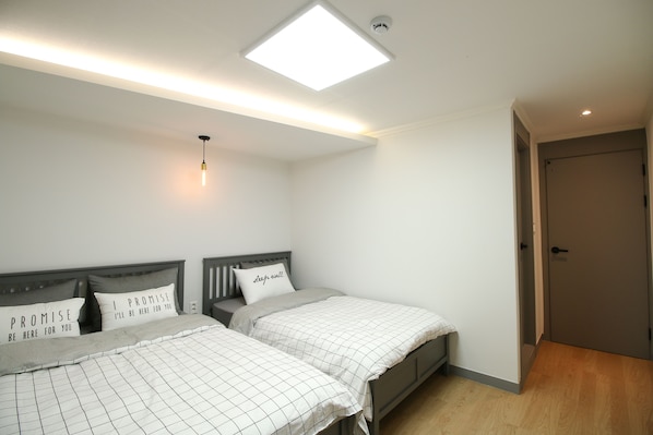 A bedroom with two beds, each with a headboard and pillows, a ceiling light, and a door.
