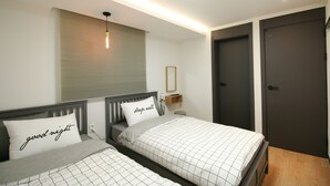 A modern bedroom with two beds, a bedside table, a nightstand, a mirror, and a door. - Heima Guesthouse Hongdae (Seoul)