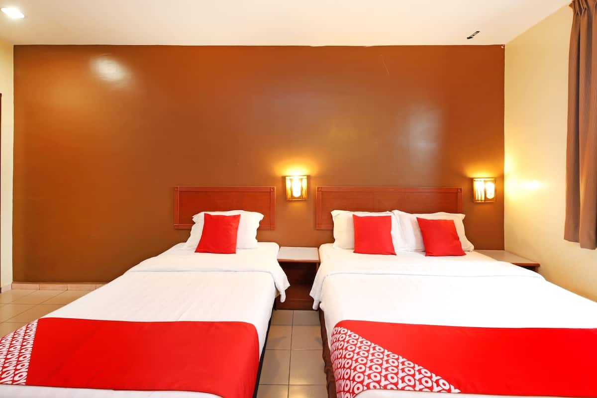 A hotel room with two beds, each with white bedding and red accents, and wall-mounted lights.