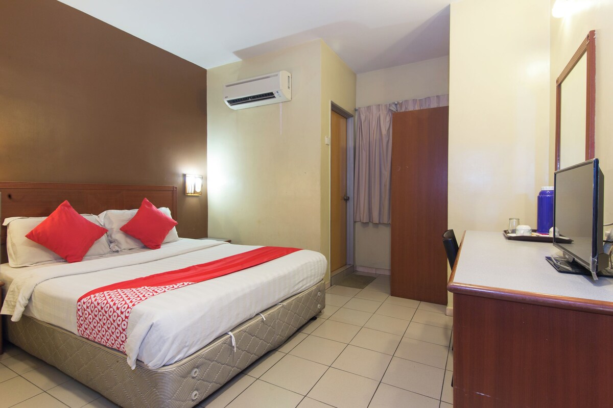 A hotel room with a bed, a desk with a computer, an air conditioning unit, and a door leading to another room.