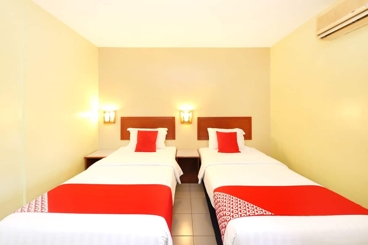 A hotel room with two single beds, each with a red and white bedspread, and two wall-mounted nightstands.