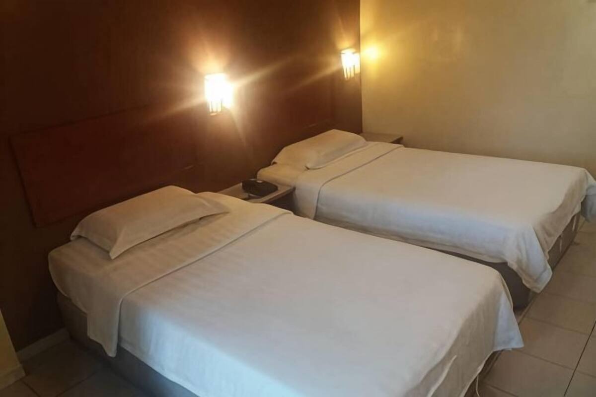 Two single beds with white linens, a wooden headboard, and wall-mounted lights.