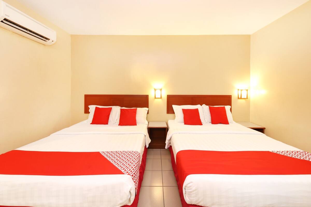 A hotel room with two beds, each with red and white bedding, and two wall-mounted nightstands.