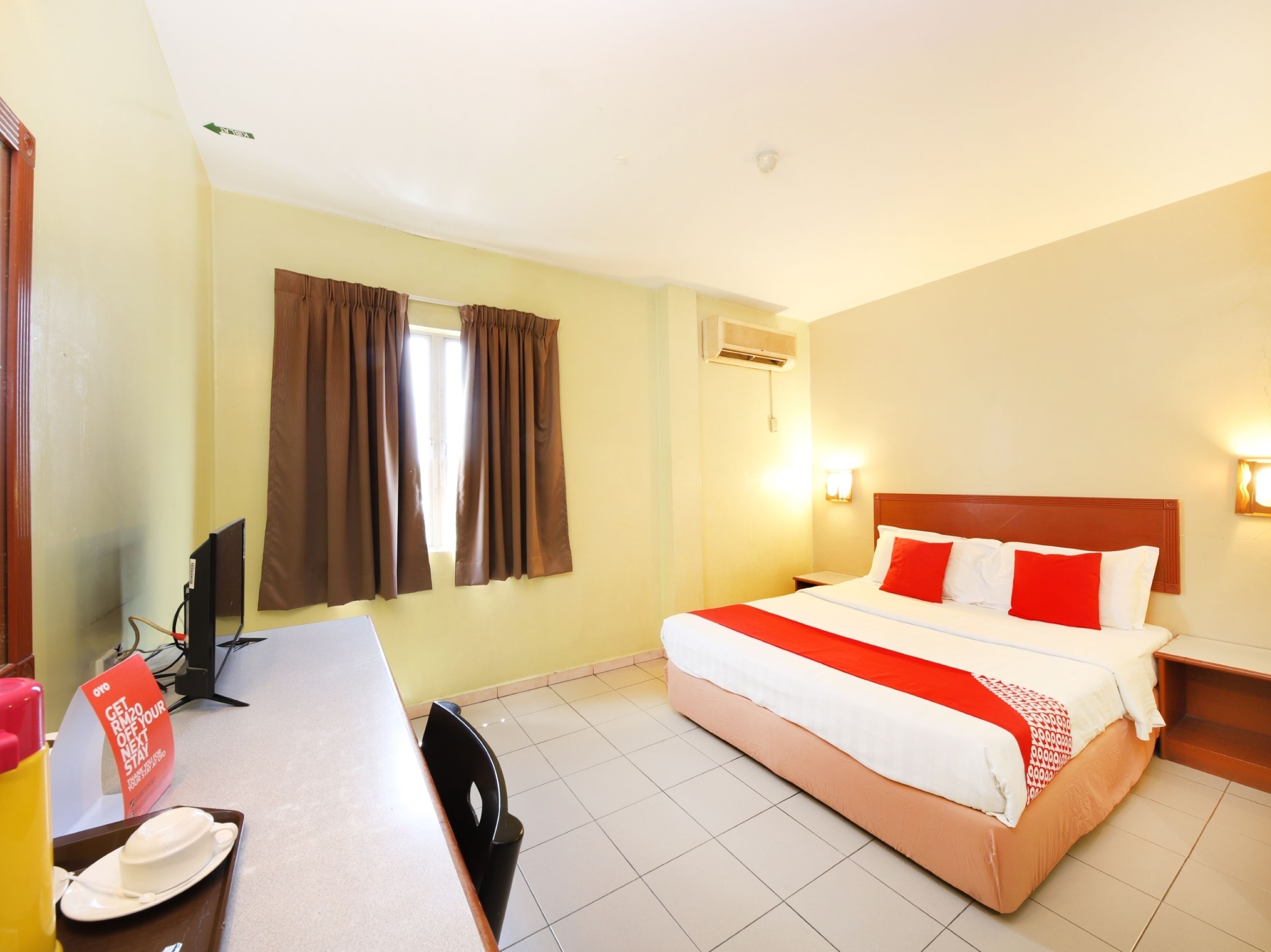 A hotel room with a bed, a desk, a chair, a TV, and a window with curtains.