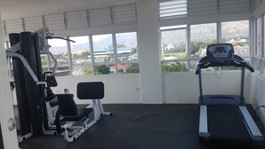 Un gimnasio con cinta de correr y máquinas de pesas, amplias ventanas con vista a la ciudad.