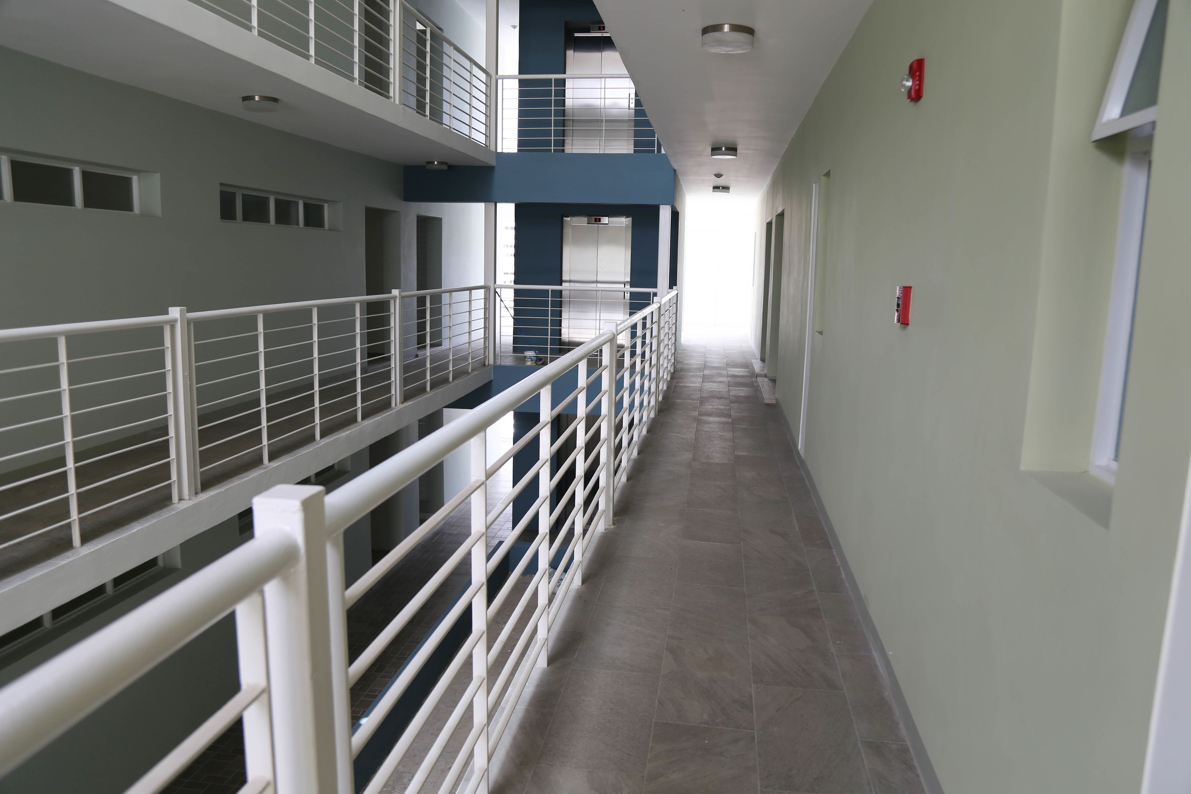 A multi-level corridor with white railings, a tiled floor, and a view of the upper level.