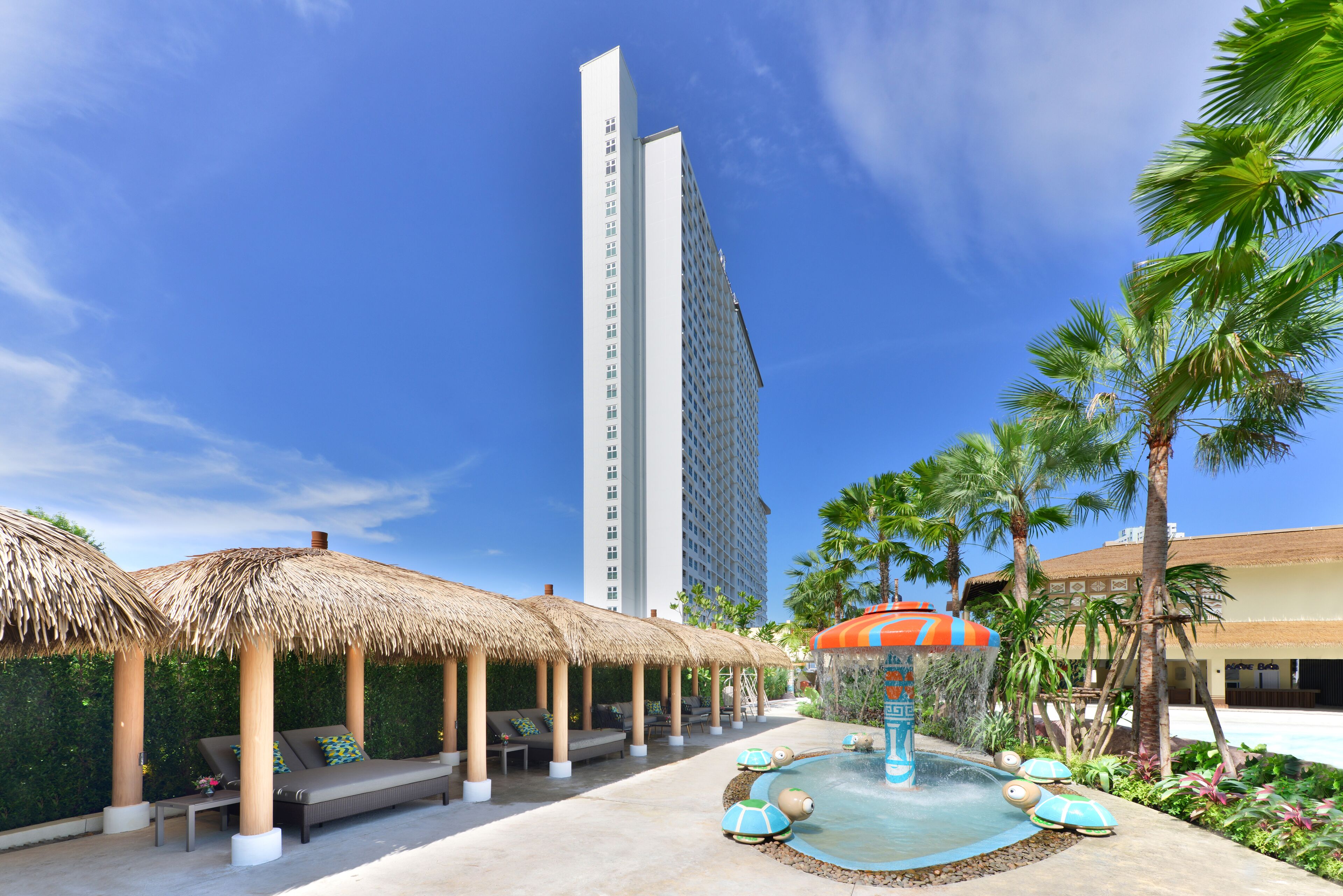 A resort pool area with thatched umbrellas, lounge chairs, and a water fountain.