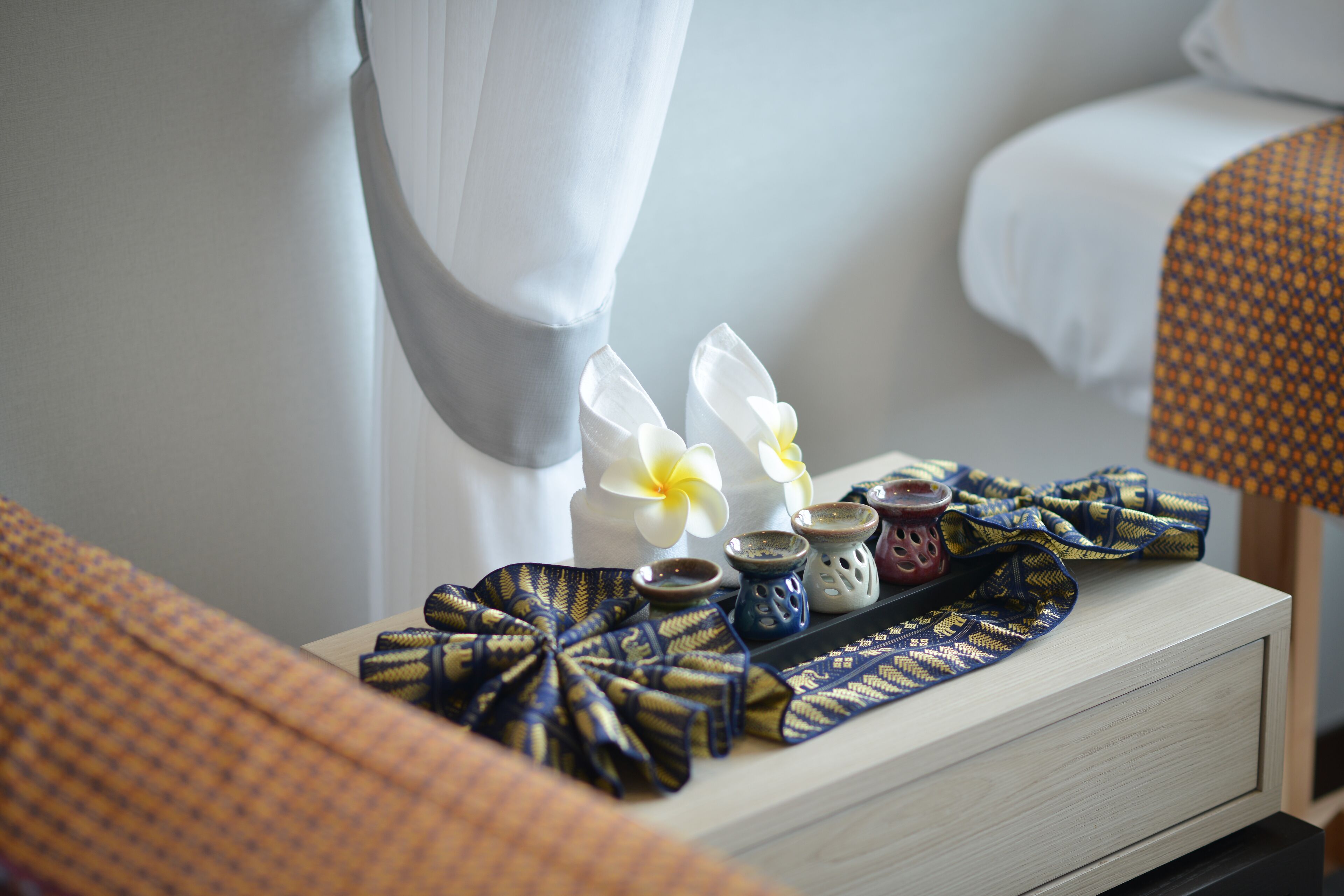 Un plateau soigneusement disposé, recouvert d’une nappe à motifs, avec deux fleurs blanches et de petits objets décoratifs, est posé sur une table de chevet dans une chambre d’hôtel.