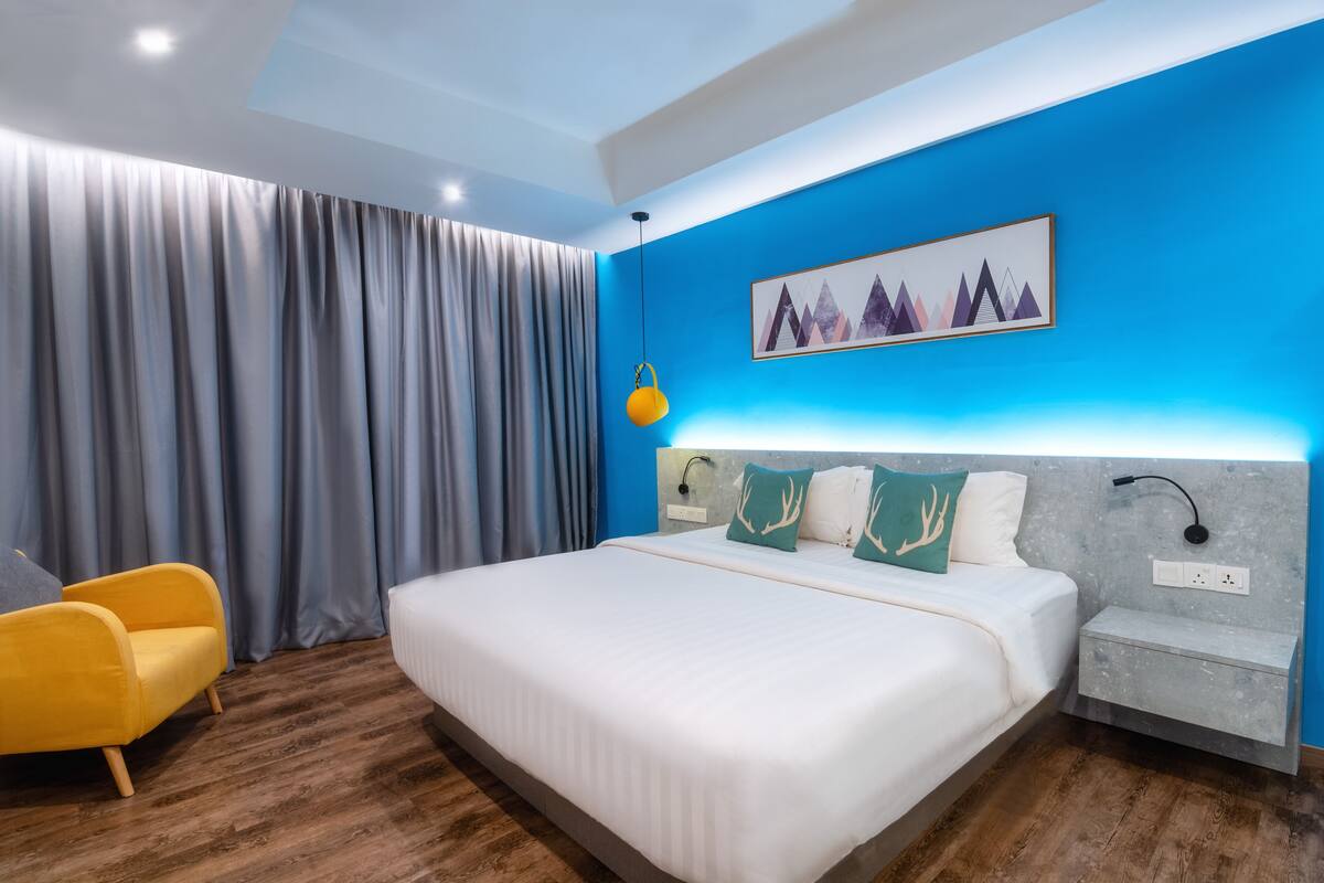 Quarto de hotel moderno com uma cama grande, uma mesa de cabeceira, uma cadeira e um quadro na parede.