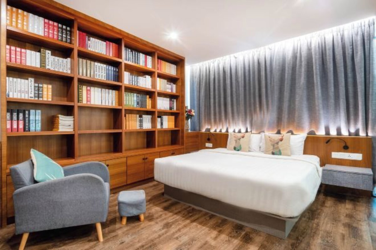 A bedroom with a large bookshelf, a bed with white bedding, and a grey upholstered armchair.