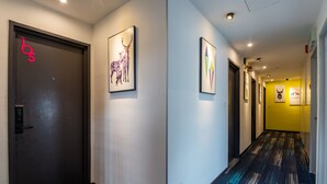 A hallway with a dark door marked with a pink 'b5' sign, a framed deer artwork, and a geometric art piece. - Apple Hotel Times Square (George Town)