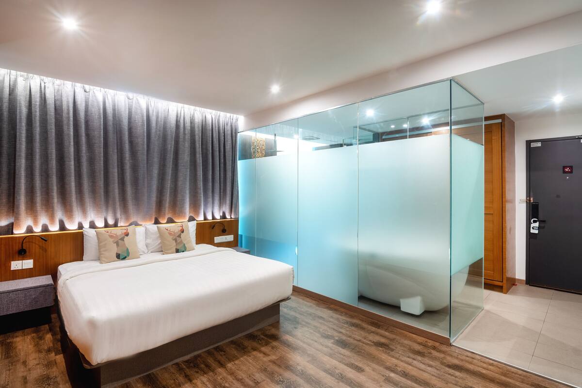 Quarto moderno com uma cama grande, uma mesa de cabeceira de madeira, um painel de vidro e uma porta escura.
