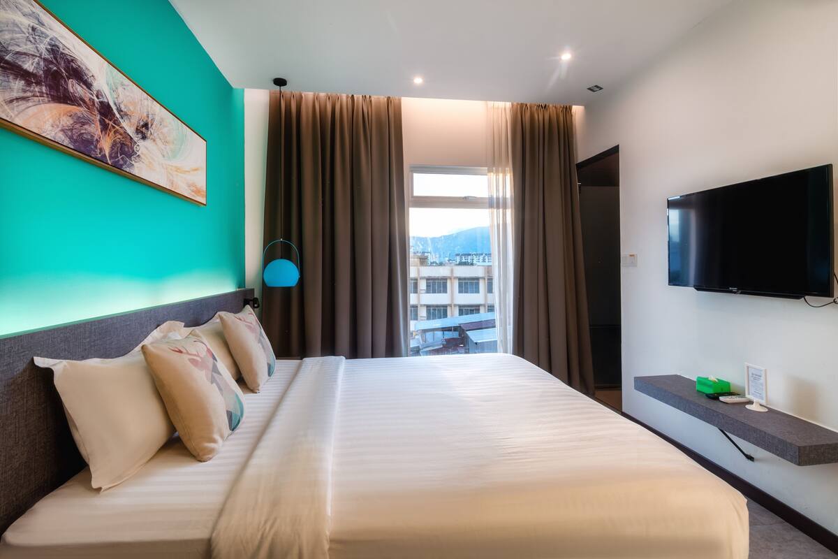 Quarto de hotel com cama grande, televisão de tela plana, janela com cortinas e um quadro na parede.