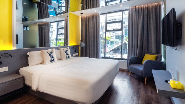 A modern hotel room with a large bed, a sofa, a TV, and a balcony view. - Apple Hotel Times Square (George Town)
