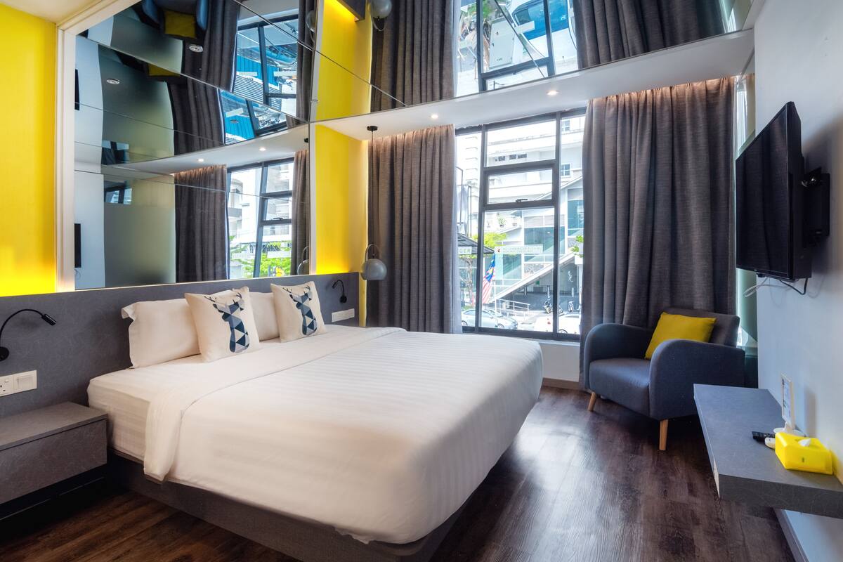 Quarto de hotel moderno com uma cama grande, um sofá, uma TV e vista para a varanda.