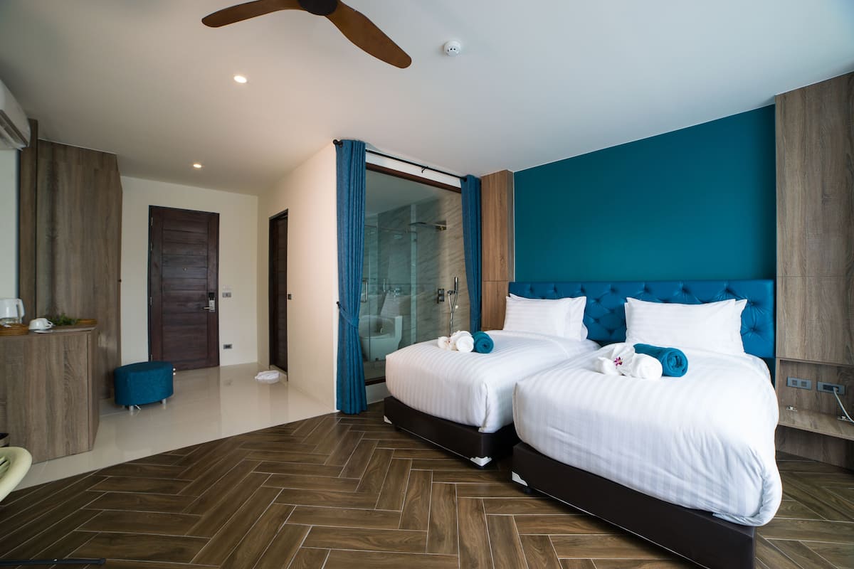 A modern hotel room with two beds, a glass shower area, and a wooden floor.