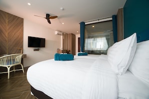 A modern hotel room with a large bed, a flat-screen TV, a ceiling fan, and a view through a glass door. - Oceana Resort Phuket (Kamala)