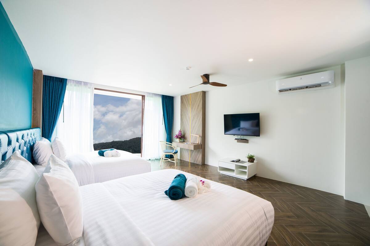 A modern hotel room with two beds, a TV, an air conditioning unit, and a view of the sky.